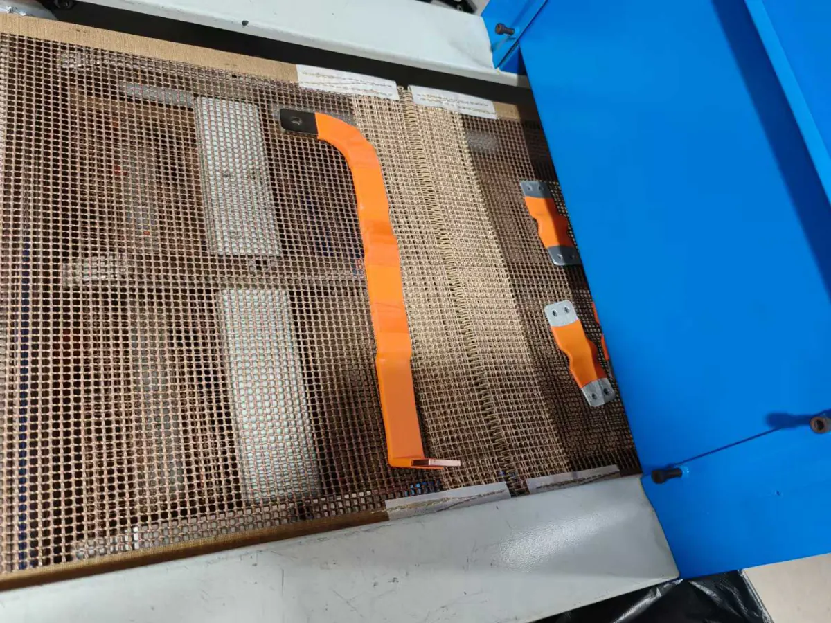 Copper busbar on a mesh conveyor belt entering the epoxy powder curing oven