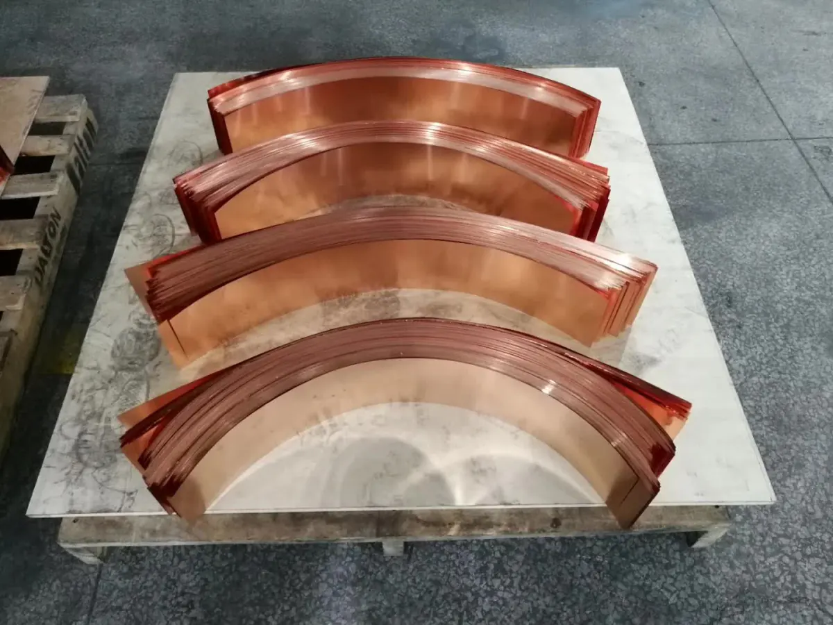 Curved laminated copper busbar stacks resting on a pallet after forming